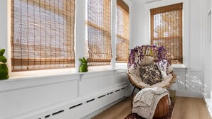Una habitación con ventanas amplias, un banco acolchado, un tapete estampado y un radiador blanco.