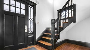 Una puerta negra con una ventana, una escalera con peldaños de madera y barandillas negras, y un piso alfombrado.