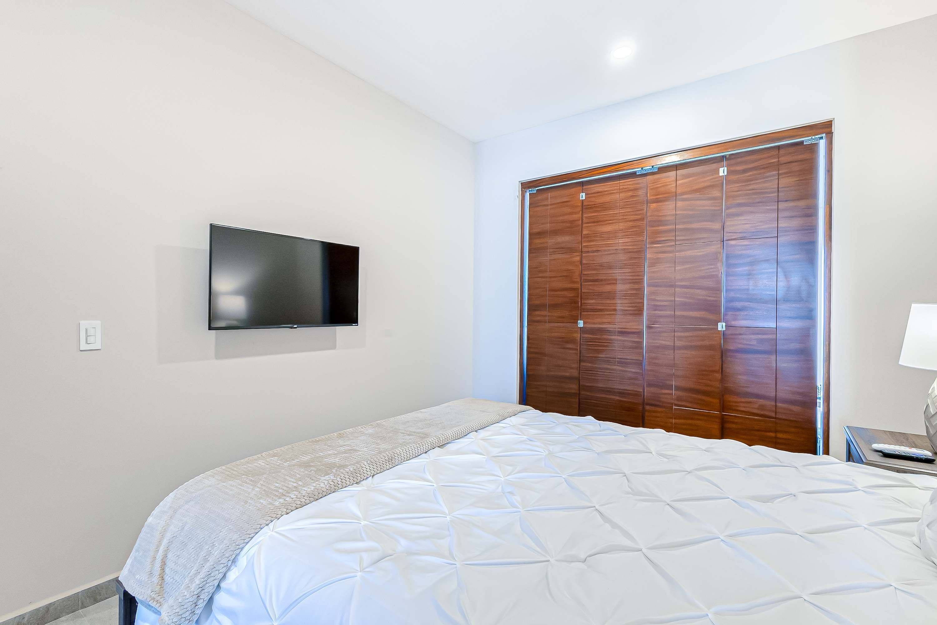 Ein Schlafzimmer mit einem Bett, einem an der Wand befestigten Fernseher und einem Holzschrank.