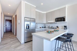 A modern kitchen with a stainless steel refrigerator, a microwave, and a large island with bar stools. - Stunning Oceanfront Luxury Apartment with spacious balcony– Perfect for Families (Cabo San Lucas)
