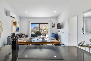 Ein moderner Essbereich mit einem Tisch für vier Personen, einer Kücheninsel mit Induktionskochfeld, einem Esstisch mit Stühlen, einer Couch und Blick auf eine Berglandschaft durch das Fenster.