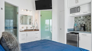 Une chambre avec un lit, une salle de bain avec une douche, une cuisine avec un four à micro-ondes et un téléviseur fixé au mur.
