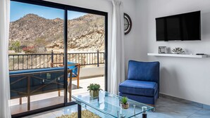 Een moderne woonkamer met een glazen salontafel, een blauwe bank, een aan de muur bevestigde televisie en een balkon met uitzicht op een bergachtig landschap.