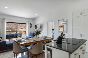 A modern dining area with a wooden table, chairs, and a glass-top kitchen island. - Morgan Residences 607A @ Boutique Hotel with pool, gym, spa (Cabo San Lucas)