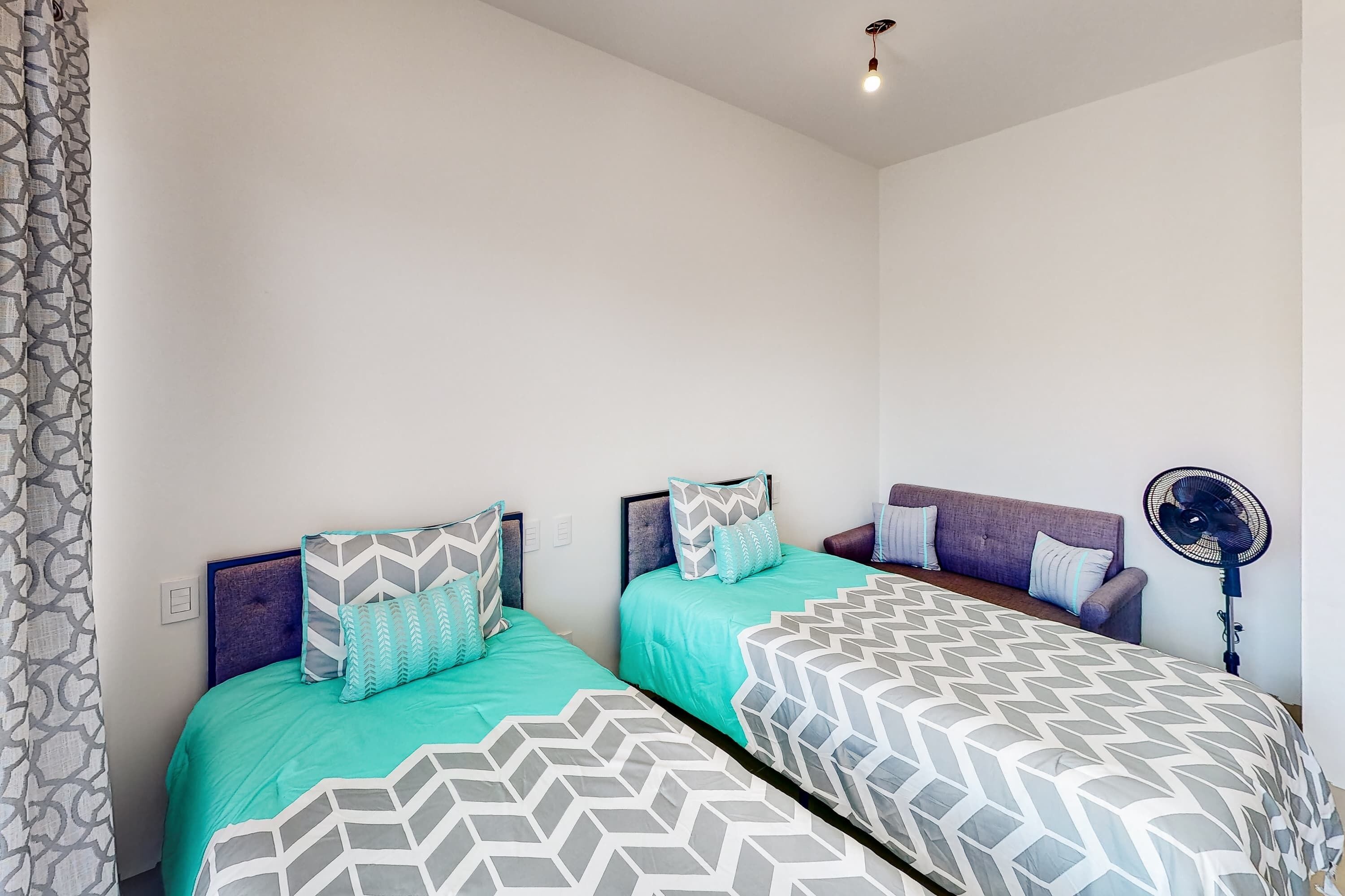 Une chambre avec deux lits, un ventilateur et un rideau à motifs.