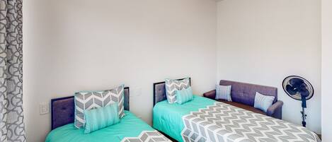 Quarto com duas camas, um ventilador e cortina estampada.