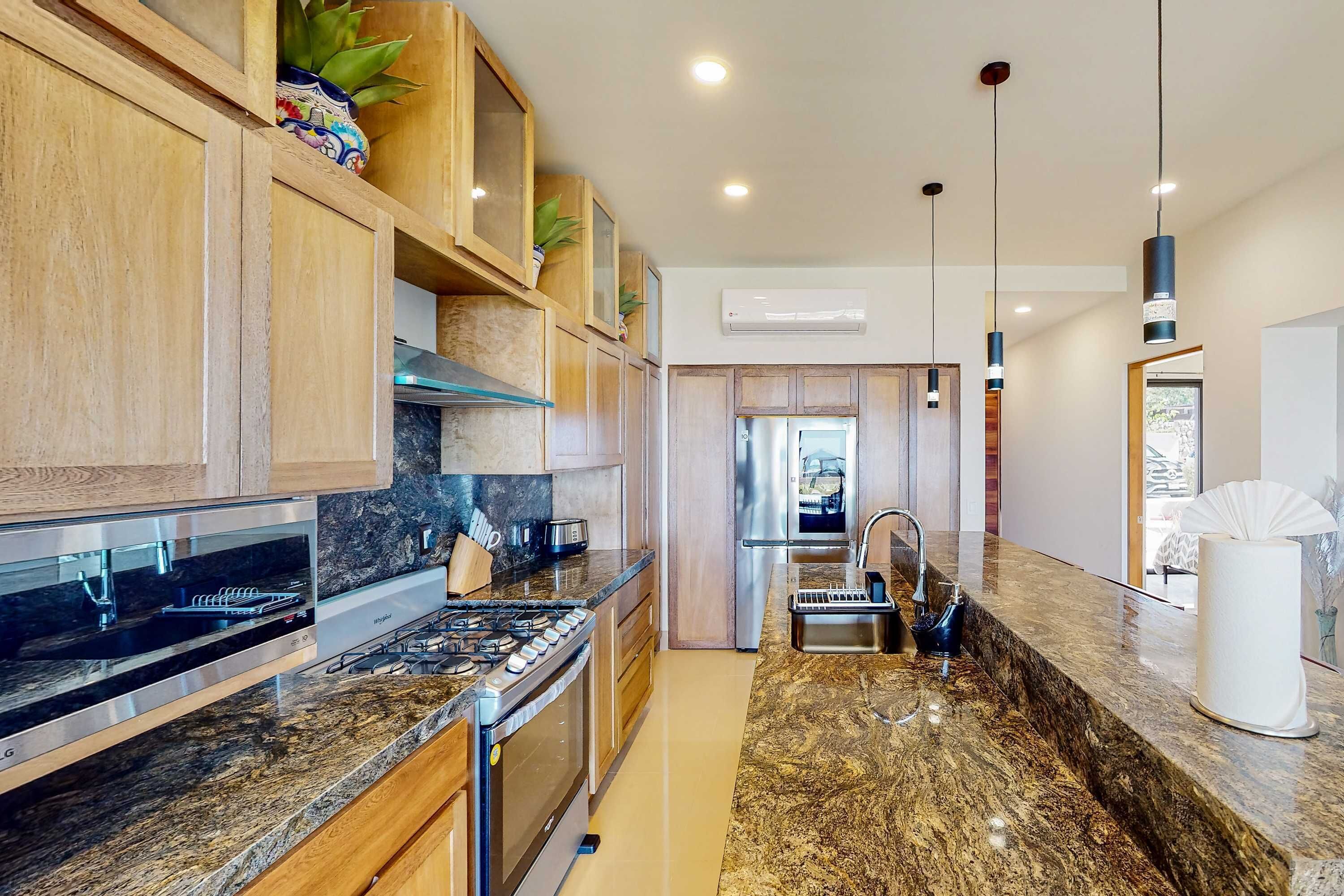 A modern kitchen with granite countertops, stainless steel appliances, wooden cabinets, and pendant lighting.