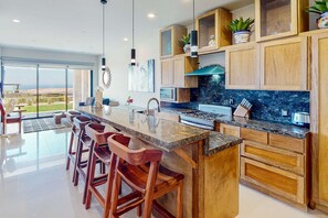 A modern kitchen with a large island, wooden cabinets, and a view of the outdoors. - Ground-floor condo with ocean view, pool, gym, hot tub, & washer/dryer (Cabo San Lucas)
