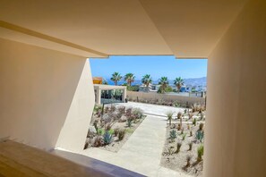A modern building with a clear view of a landscaped courtyard featuring various plants and a pathway. - Charming 2 BR Condo | Ocean Views, Pool & Gym (Cabo San Lucas)