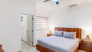 Ein Schlafzimmer mit einem Bettgestell aus Holz, zwei Nachttischen mit Lampen, einem Deckenventilator und einem Fenster mit Jalousien.