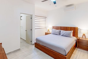 Ein Schlafzimmer mit einem Bettgestell aus Holz, zwei Nachttischen mit Lampen, einem Deckenventilator und einem Fenster mit Jalousien.