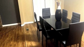 Un comedor con una mesa y sillas negras, un florero con planta y una puerta al fondo.