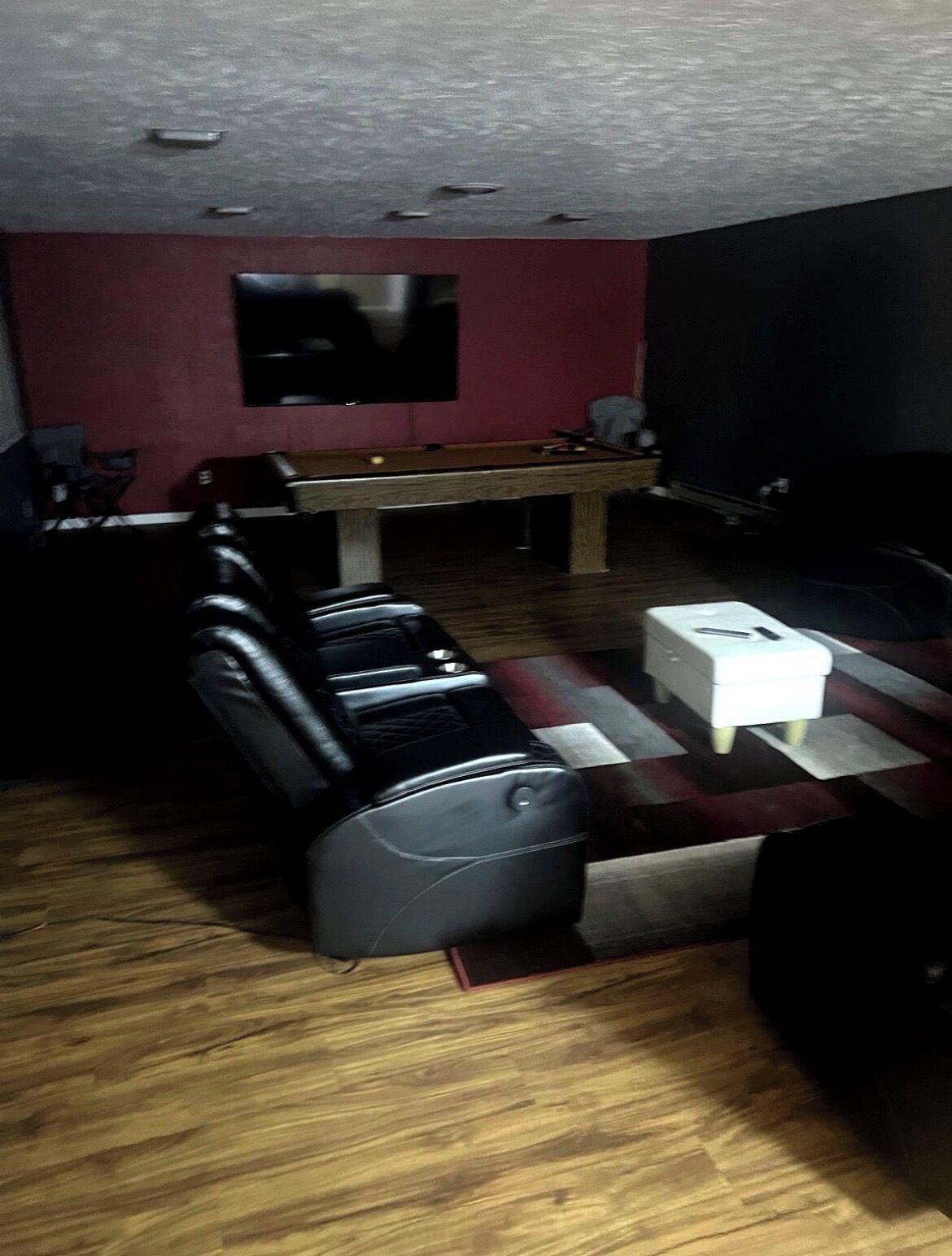 A room with a pool table, a flat-screen TV mounted on the wall, and a seating area with leather sofas.