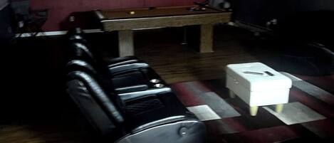 A room with a pool table, a flat-screen TV mounted on the wall, and a seating area with leather sofas.