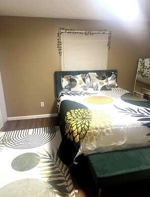 Une chambre à coucher comprenant un lit, une table de chevet, une fenêtre avec des stores et un luminaire fixé au mur.