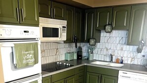 Una cucina con mobili verdi, un forno a microonde bianco, un piano cottura e una lavastoviglie.