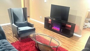 Una sala de estar con un sofá de cuero negro, una mesa de centro de vidrio, un sillón negro y un mueble de televisión con chimenea.