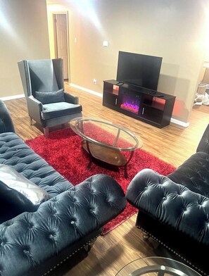 Ein Wohnzimmer mit einer schwarzen Ledersofa, einem Glastisch, einem schwarzen Sessel und einer TV-Konsole mit Kamin.