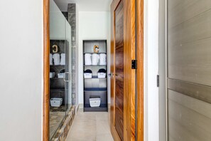 A hallway with a wooden door, a glass door, and a shelf with towels and baskets. - Modern studio with rooftop lounge, pools, gym, pickleball & Netflix access (Cabo San Lucas)