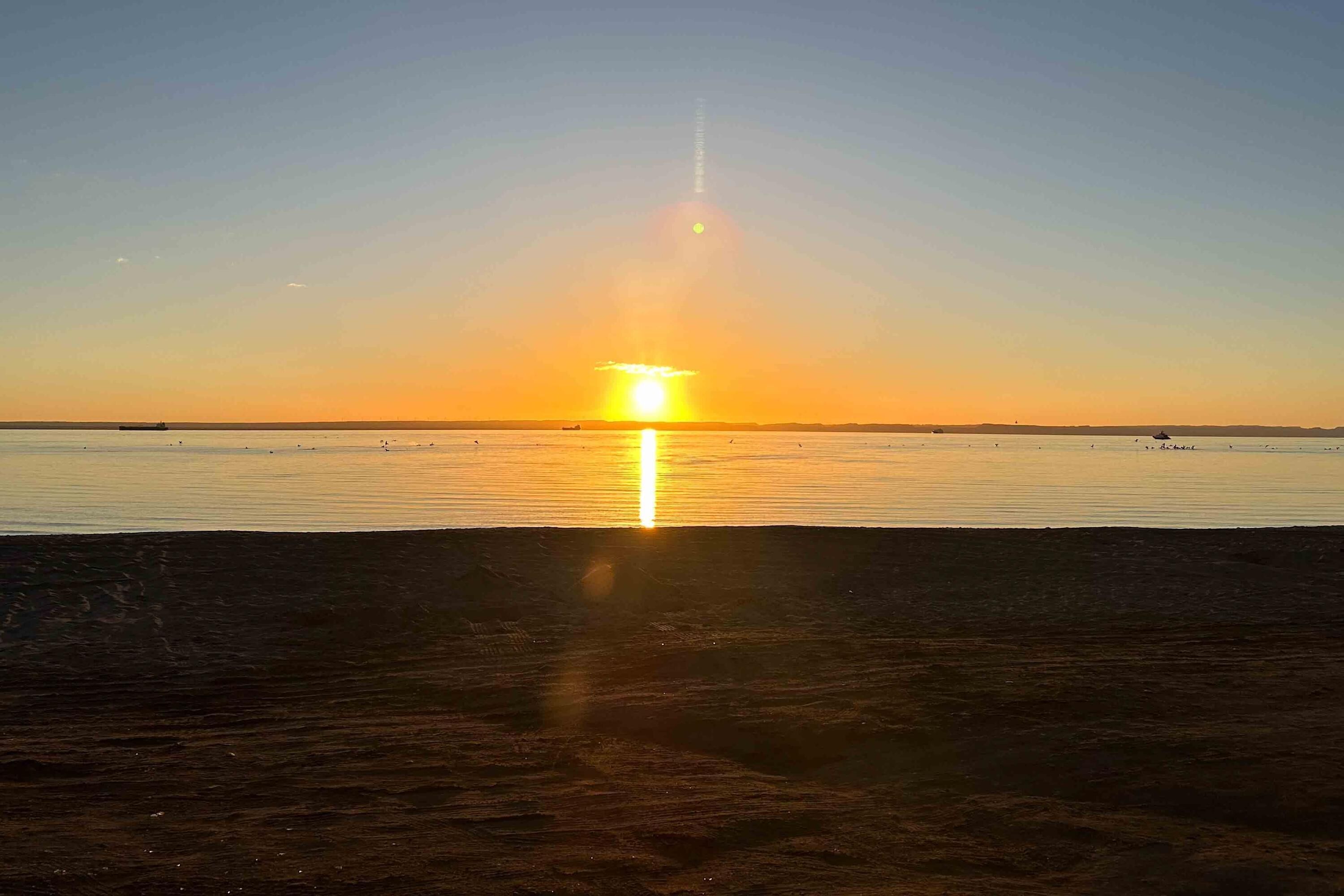 Ein Sonnenuntergang über ruhigem Wasser mit einer fernen Küste.