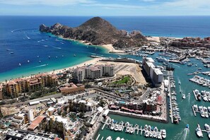 A coastal town with a marina, buildings, and a prominent hill. - Modern studio with rooftop lounge, pools, gym, pickleball & Netflix access (Cabo San Lucas)