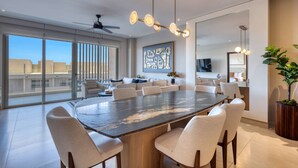 Un'area pranzo moderna con un tavolo grande, sedie, una ventola a soffitto e un'ampia finestra con vista sulla città.