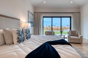 A hotel room with a large bed, a view of the outdoors, a chair, and a table. - Luxury Diamante Retreat - Pool & World-Class Golf (Cabo San Lucas)