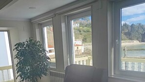 Une pièce avec un canapé, une plante en pot et de grandes fenêtres donnant sur une plage et des bâtiments.