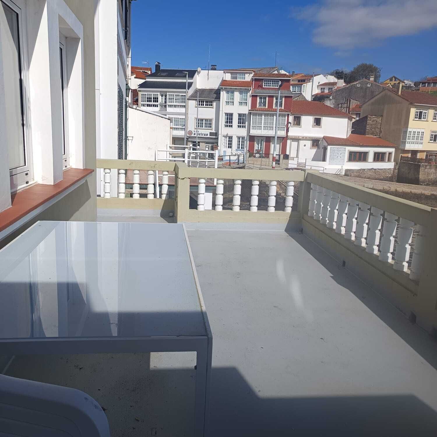 A balcony with a table and chairs, overlooking a row of buildings with red roofs.