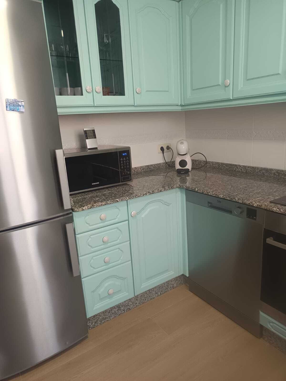 A kitchen with teal cabinets, a stainless steel refrigerator, a microwave, and a dishwasher.
