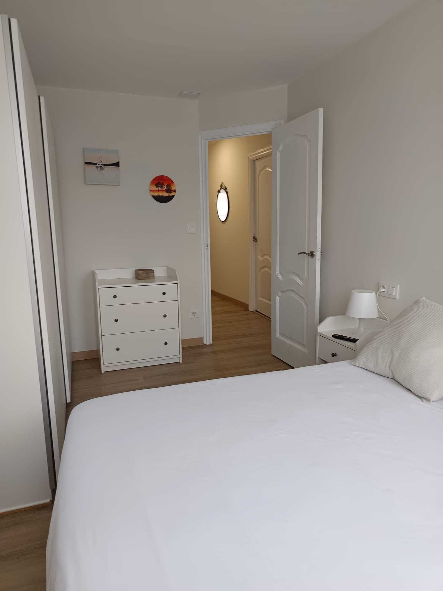 A bedroom with a bed, a dresser, a nightstand, a mirror, and a door leading to another room.