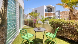 Eine moderne Terrassenanlage mit Tisch und Stühlen, einer Glastrennwand und Blick auf ein weißes Gebäude.
