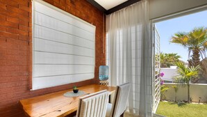 Ein Zimmer mit einem Holztisch, zwei Stühlen, einem Wasserspender und Blick auf einen Garten mit Palmen und Blumen.