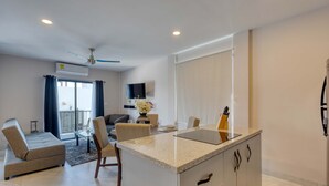 Una cocina moderna con una isla central, una zona de comedor con mesa y sillas, un sofá y un balcón con vistas.