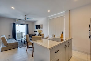 A modern kitchen with a central island, a dining area with a table and chairs, a sofa, and a balcony with a view. - Dog-friendly apartment with rooftop infinity pool, gym, central AC, & balcony (Cabo San Lucas)
