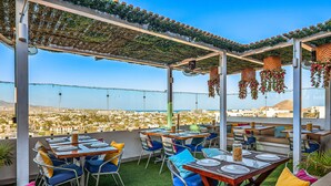 Una terraza al aire libre con mesas y sillas, vistas a la ciudad y decoraciones colgantes.