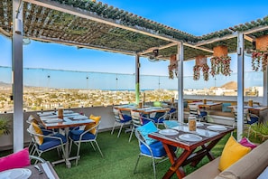 An outdoor terrace with tables and chairs, a view of the city, and hanging decorations. - Dog-friendly apartment with rooftop infinity pool, gym, central AC, & balcony (Cabo San Lucas)