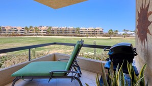 Uma varanda com espreguiçadeira, churrasqueira e vista para um campo de golfe e edifícios.