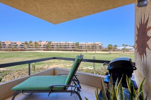 Ein Balkon mit Liegestuhl, Grill und Blick auf einen Golfplatz sowie Gebäude.