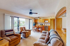 A living room with a sofa, armchair, and a dining table with chairs. There is a kitchen area with wooden cabinets and a microwave. - Inviting apartment across from the beach with pool, grill, balcony & golf nearby (San José del Cabo)