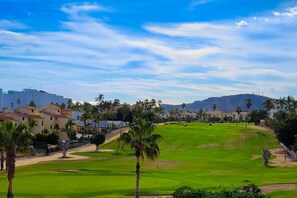 A golf course with a clear sky, palm trees, and buildings in the background. - Inviting apartment across from the beach with pool, grill, balcony & golf nearby (San José del Cabo)