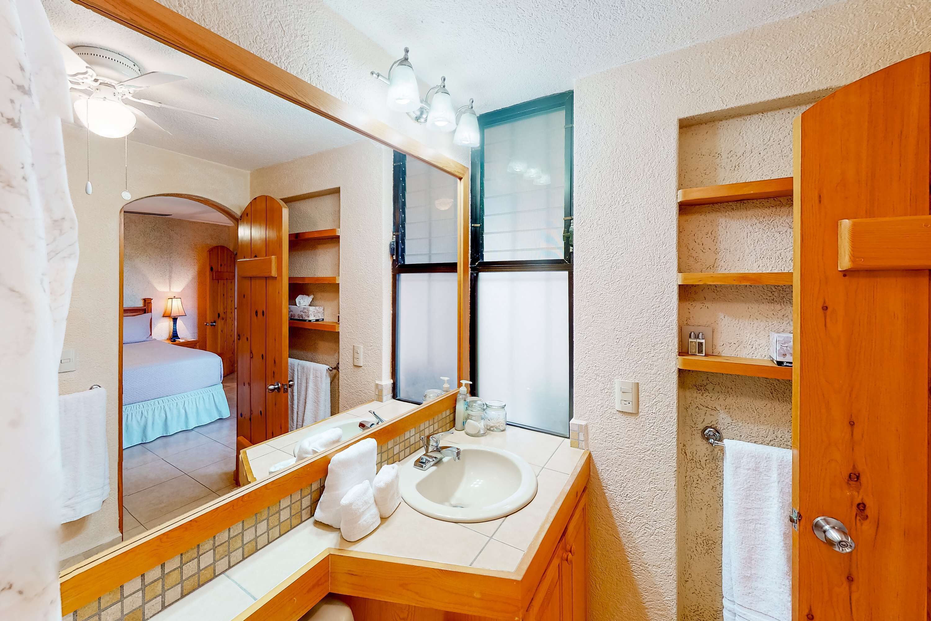 A bathroom with a large mirror, a sink, a shower, and wooden shelving.