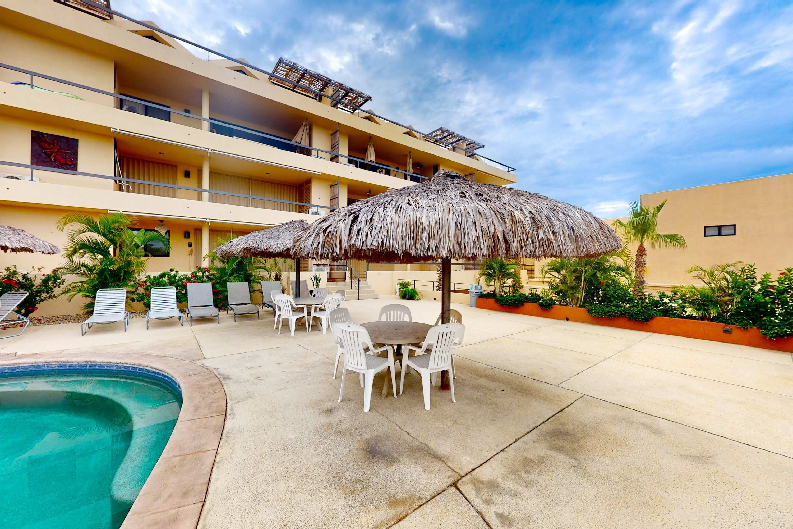 A hotel courtyard with a swimming pool, outdoor seating, and thatched umbrellas.