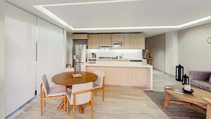 Eine moderne Küche mit Kochinsel, ein Essbereich mit rundem Tisch und ein Wohnbereich mit Sofa und Couchtisch.