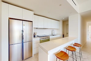 A modern kitchen with white cabinetry, a stainless steel refrigerator, a stove, and a marble countertop. - Spacious 2 BR Condo | City Views & Pool (Cabo San Lucas)