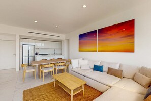 A modern living room with a sofa, coffee table, and dining area. - Spacious 2 BR Condo | City Views & Pool (Cabo San Lucas)