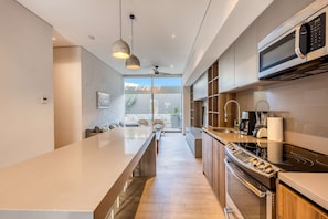 A modern kitchen with a long island, stainless steel appliances, pendant lighting, and a view to the outdoors. - Modern marina-view penthouse with private hot tub, pool & Netflix (Cabo San Lucas)