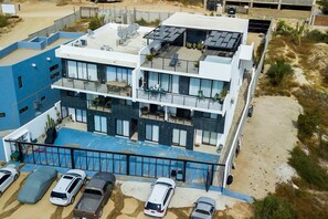 A multi-story hotel with a rooftop terrace, a swimming pool, and a parking area. - Ocean view condo with scenic balcony, well-equipped kitchen, internet, & W/D (Cabo San Lucas)