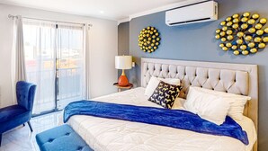 Ein modernes Schlafzimmer mit einem großen Bett, einem blauen Hocker, einem Sessel und einer Wanddekoration.