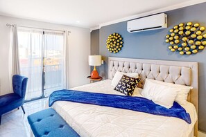 A modern bedroom with a large bed, a blue ottoman, a chair, and a decorative wall piece. - Cerro Colorado Condo | Condo in Cabo San Lucas (Cabo San Lucas)